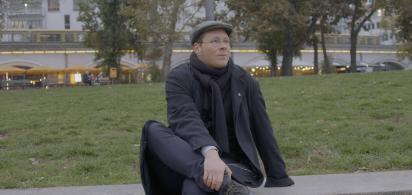 Person mit Mütze und dunkler Kleidung sitzt in einem Park