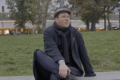 Person mit Mütze und dunkler Kleidung sitzt in einem Park