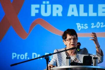 Rita S&uuml;ssmuth am Redepult, Hintergrund: eine rote Aidsschleife und die Schrift 