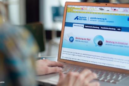 Person sitzt vor einem Laptop. Zu sehen ist die Website der Onlineberatung der Deutschen AIDS-Hilfe.