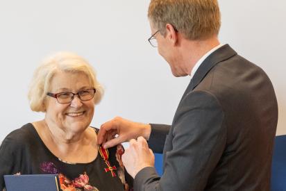 Daniel Günther steckt Hildegard Welbers das Bundesverdienstkreuz an